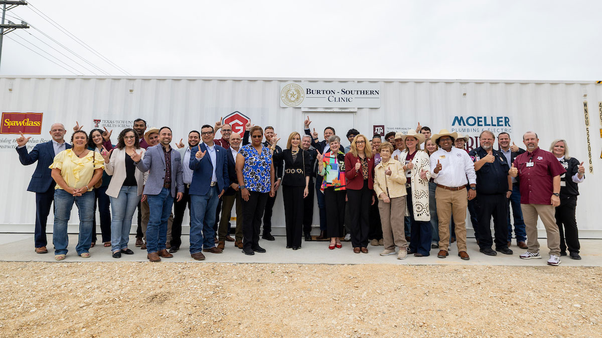 Professionals pose for a large group photo in front a shipping container converted into a medical clinic branded "Burton - Southern Clinic."