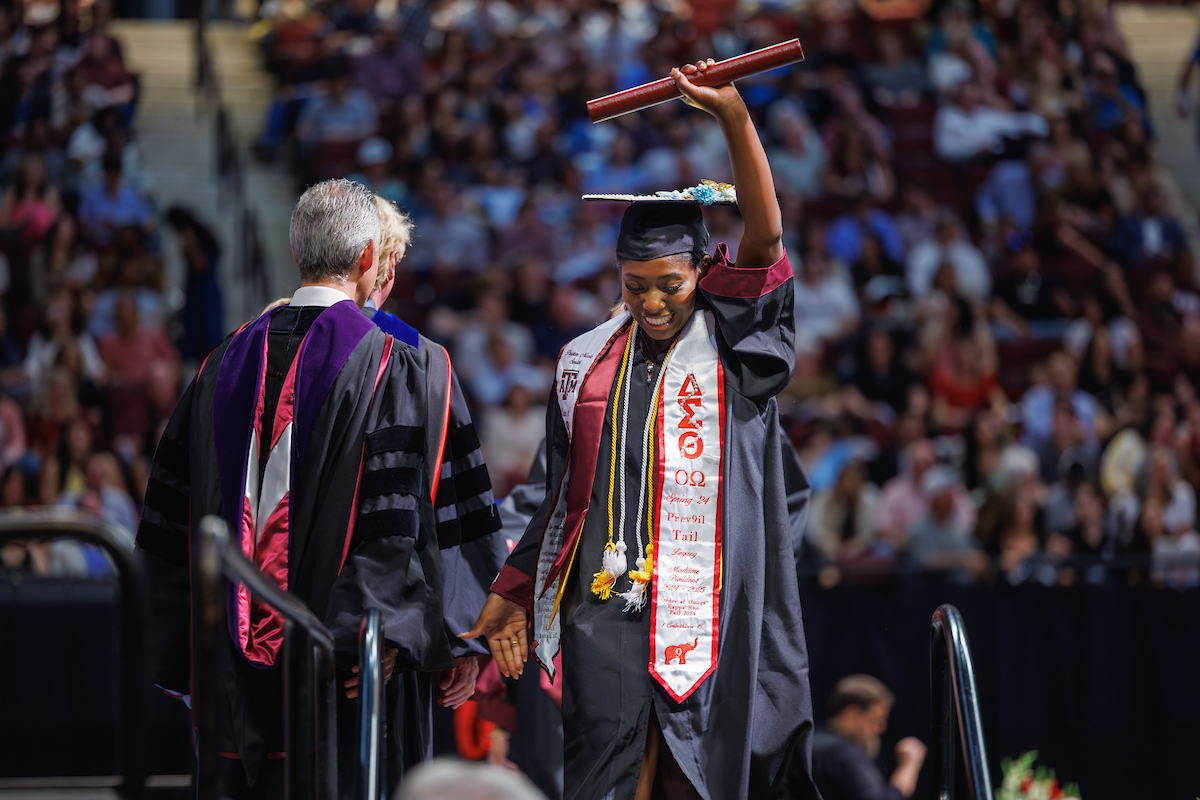 Student graduating holding up diploma in a cap and gown.