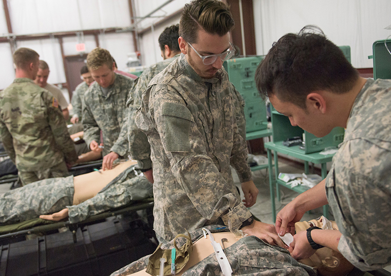 Two men in fatigues examining a manikin in a field hospital